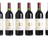 six bottles of red wine lined up on a white surface