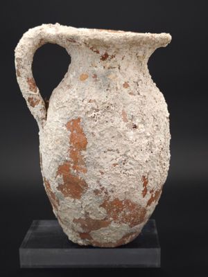 un vase blanc et marron muni d'une anse, posé sur un socle noir