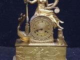 a gold clock with a woman sitting on top of it