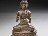 statue en bronze représentant un Bouddha assis sur un socle blanc
