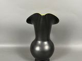 un vase noir surmonté d'un couvercle jaune, posé sur une surface blanche