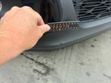 a person measuring the width of a car ' s front bumper