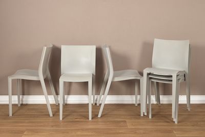 trois chaises blanches placées devant un mur marron dans une pièce