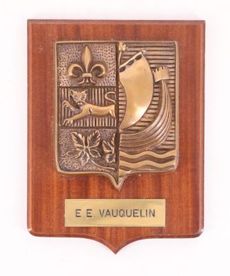 une plaque en bois sur laquelle figurent un bateau et une fleur, avec en dessous une autre plaque portant l'inscription « e e vauguelin »