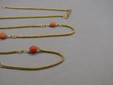 three gold chains with orange beads on them sitting on a table