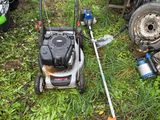 une tondeuse à gazon posée dans l'herbe, près d'une clôture