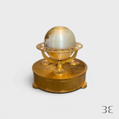 un globe doré et blanc posé sur un socle, sur fond blanc
