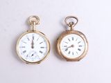 two gold pocket watches sitting side by side on a white surface