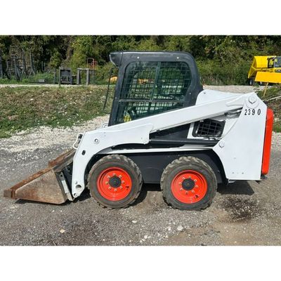 a picture of a small ski - loader parked in a gravel lot