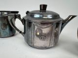 two silver teapots and a sugar bowl on a white surface