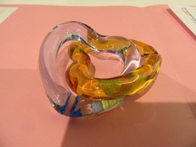 un objet en verre en forme de cœur posé sur une surface rose