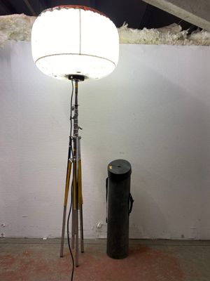 a lamp that is on a tripod next to a trash can