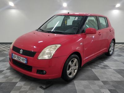 une Suzuki Swift rouge garée sur un sol à damier dans un garage