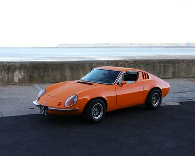 an orange sports car parked on the side of a road next to the ocean