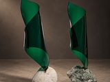 une paire de sculptures en verre vert posées sur un rocher blanc