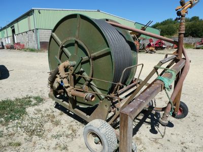 un grand arroseur vert posé sur un chariot, dans la terre