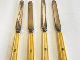 Quatre couteaux sont alignés sur une table, sur fond blanc.