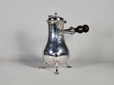 une cafetière ancienne en métal argenté, munie d'une anse et posée sur un socle