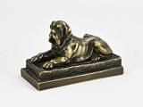 une statue en bronze représentant un chien couché, posée sur un socle en bois