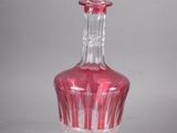 une carafe en verre rose avec un bouchon transparent, posée sur une surface blanche