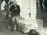 photo en noir et blanc d'un homme debout devant une maison avec un chien