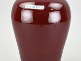 a red vase with a tag on it sitting on a table