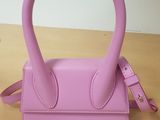 sac à main en cuir rose avec une poignée et une bandoulière, posé sur une table en bois