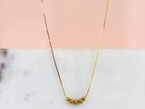 un collier en or orné de trois perles, posé sur une surface en marbre