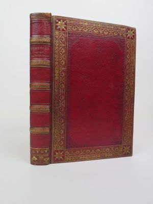 un vieux livre avec une couverture rouge et des bordures dorées sur fond blanc