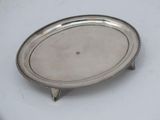 an oval silver tray with a beaded edge on a white surface