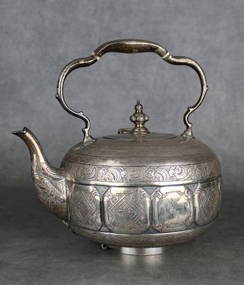 une vieille théière en argent avec une anse, posée sur une table