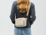 une femme vue de dos, vêtue d'un pull gris et d'un jean, avec un sac à bandoulière blanc