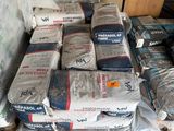 de nombreux sacs de ciment posés par terre à côté d'une pile de cartons