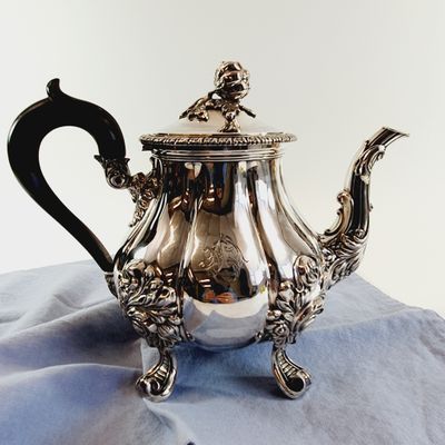 a silver tea pot sitting on top of a blue cloth