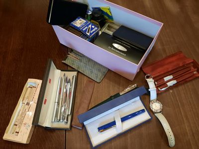 a box of pens, a watch, a wallet, and other items on a table