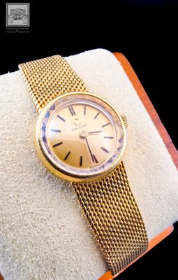 a gold watch on a gold bracelet on a white pillow
