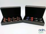 deux paires de bagues de manchette dans un coffret noir posé sur une surface blanche