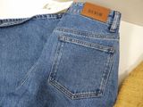 denim pants with a leather label on a hanger on a white surface