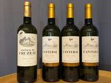 four bottles of wine are lined up on a wooden barrel