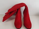 une paire de bottes en daim rouge posées sur une surface blanche, à côté d'une plante