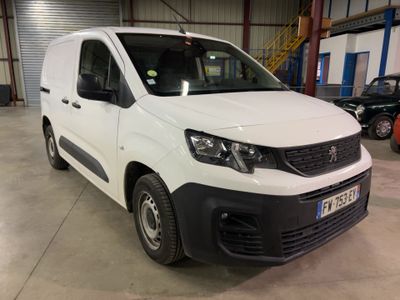 La camionnette blanche est garée dans un grand entrepôt, à côté d'autres voitures.