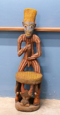une statue en bois représentant un homme assis sur une chaise