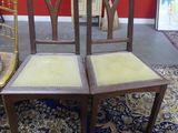 pair of antique wooden chairs with upholstered seats in front of a red wall