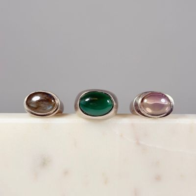 trois bagues en argent ornées de pierres vertes et roses, posées sur une surface en marbre