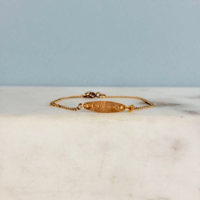 un bracelet en or orné d'un poisson, posé sur une surface en marbre