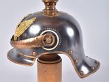 an old helmet with a gold decoration on top of a wooden base