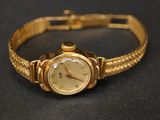 une montre en or montée sur un bracelet en or, posée sur une surface noire