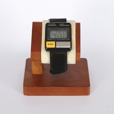 une montre numérique posée sur un socle en bois, sur fond blanc
