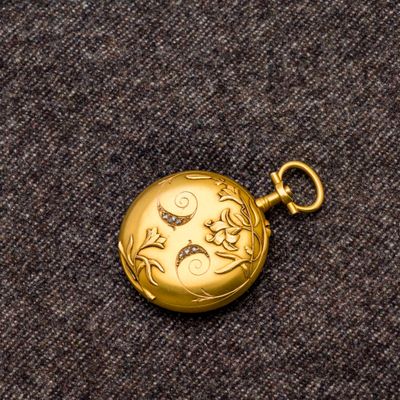 une petite montre de poche en or posée sur un tissu marron