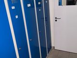 Plusieurs casiers bleus sont alignés dans une pièce dont la porte est blanche.